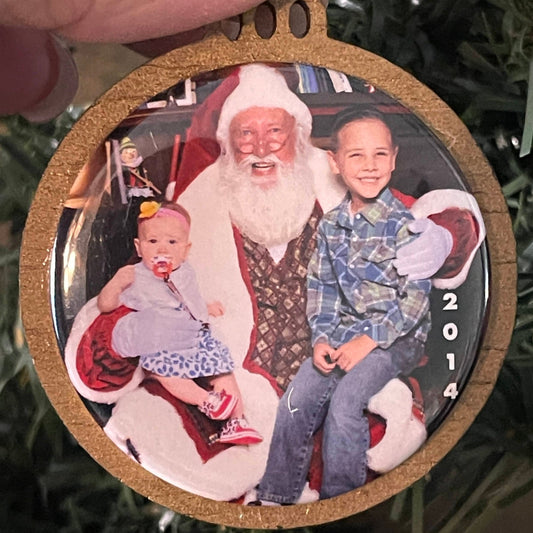 Round photo ornament with family picture held by a hand against a Christmas tree background